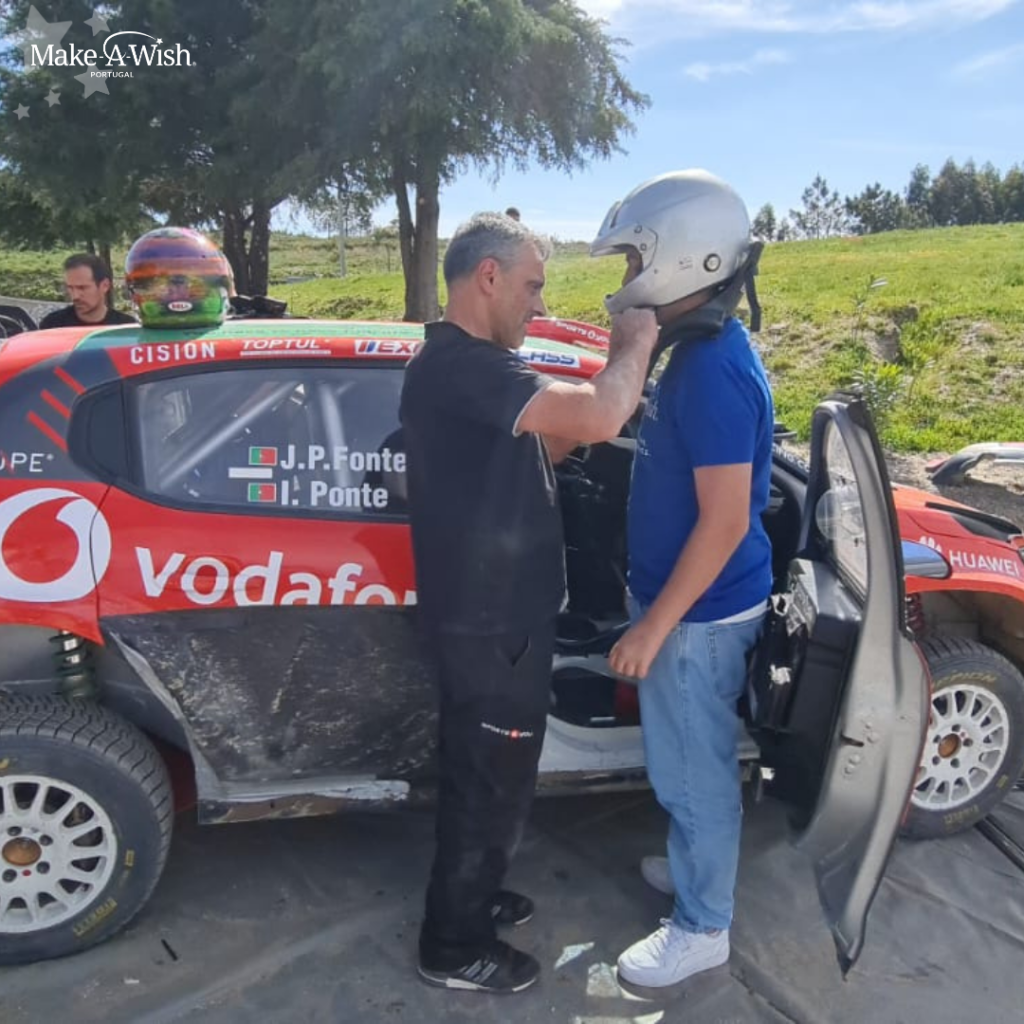 Homem aperta capacete de Duarte Silva, estão junto ao carro de rally