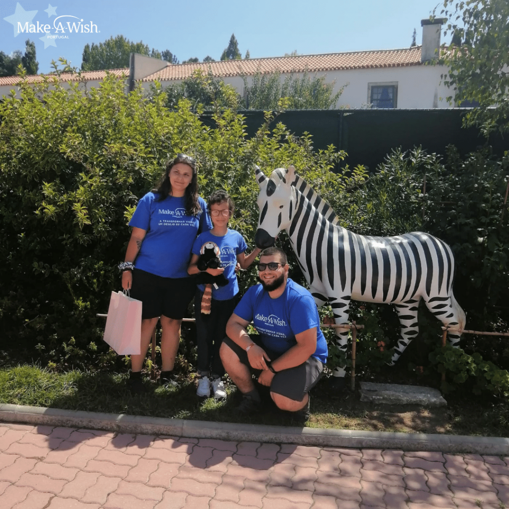 Rosana, dois voluntários Make-A-Wish a pousar à frente de uma estátua de uma zebra